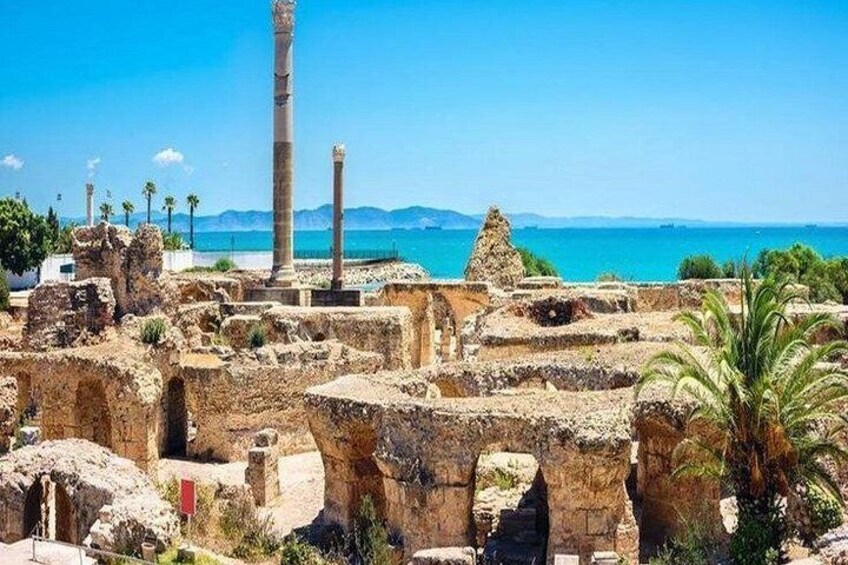 Rovine antiche con colonne e archi, un cielo azzurro limpido e una costa sullo sfondo. 3