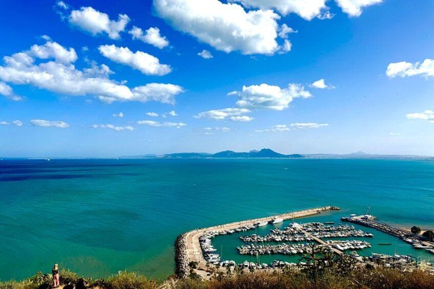 Una marina costiera con barche, una diga frangiflutti rocciosa e un cielo azzurro limpido. 4