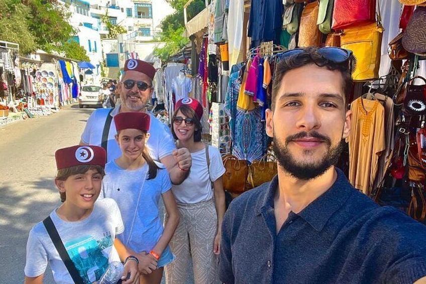 Un mercato rionale con persone che indossano cappelli tradizionali, tessuti colorati e una varietà di merci in vendita. 3