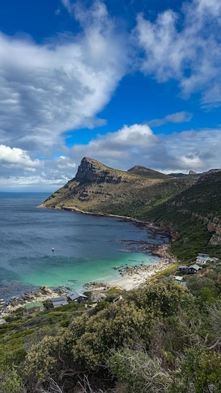 A coastal landscape with a prominent mountain, clear blue sea, and a small settlement with houses. 5