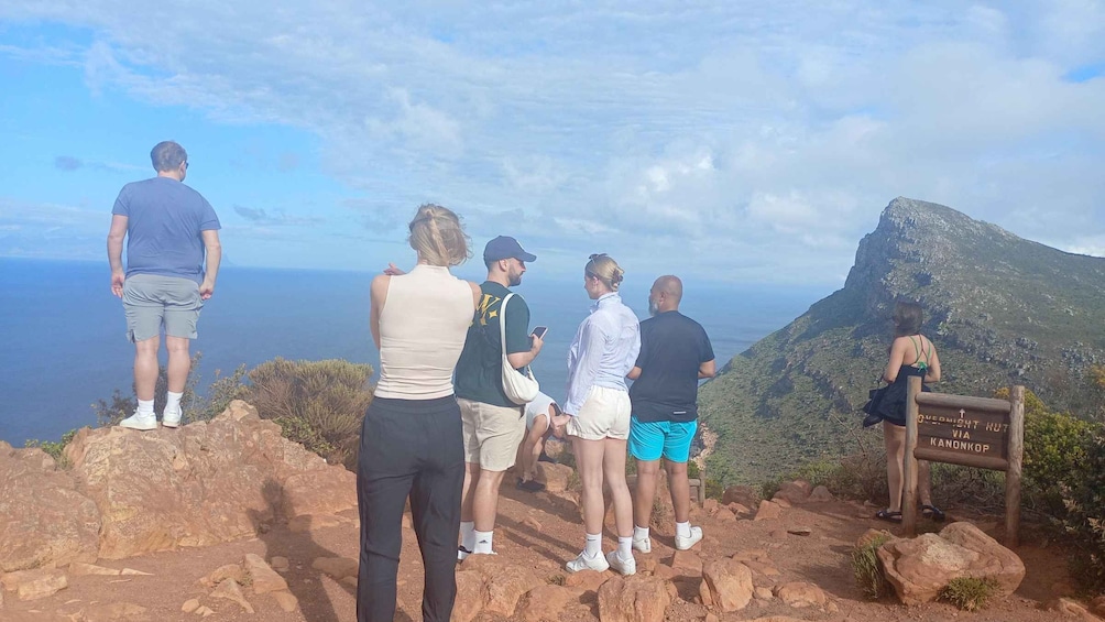 A group of people standing on a rocky outcrop overlooking a coastal landscape with a mountain in the distance. 2