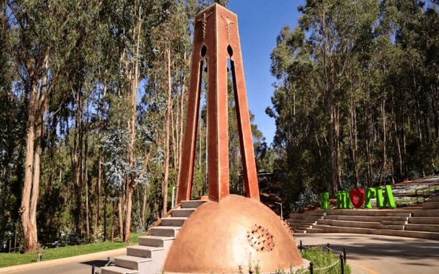 A large red tower with a dome base, surrounded by a forested area and a staircase leading up to it. 2