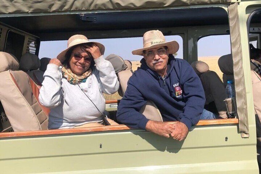 Two people seated in a vehicle with a desert landscape in the background. 3
