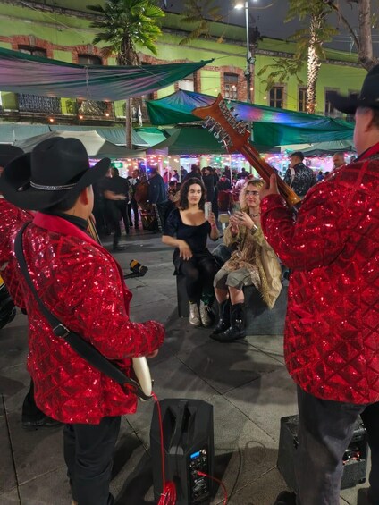 A lively outdoor event with people in red sequined jackets, a microphone stand, and a speaker. 1