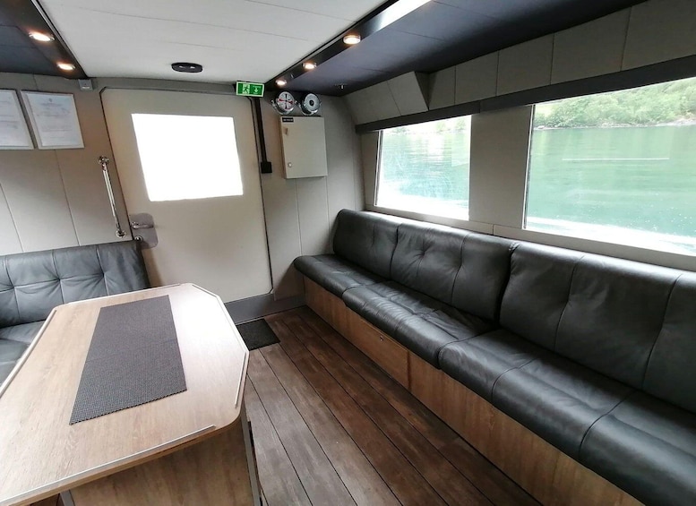 A cabin interior with a wooden table, a cushioned bench, and a window overlooking water. 4