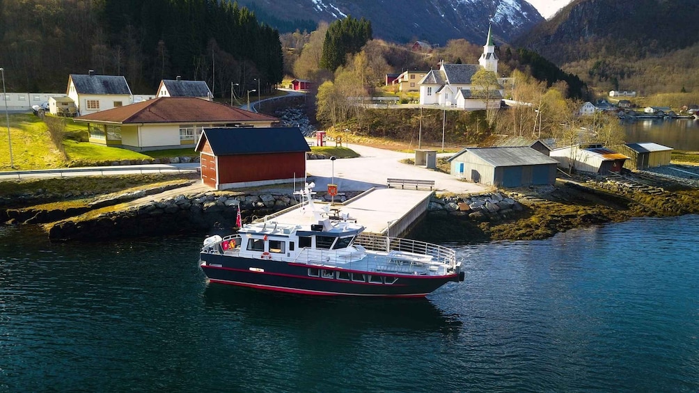 A boat docked at a pier with a mountainous backdrop and a small village. 1