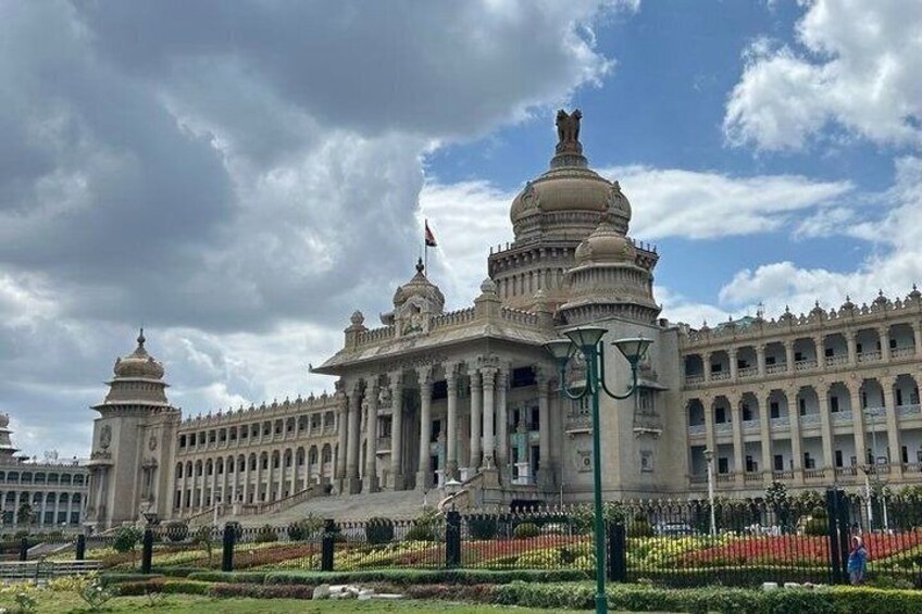 Un grande edificio decorato con tetti a cupola e colonne, circondato da un giardino curato e da un recinto. 2