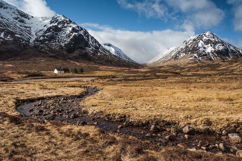 A mountainous landscape with a small white building, a stream, and a clear sky. 5