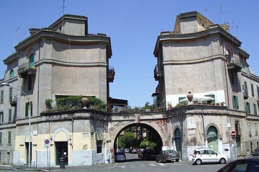 A large stone archway with two buildings on either side, a street with cars, and a clear blue sky. 3