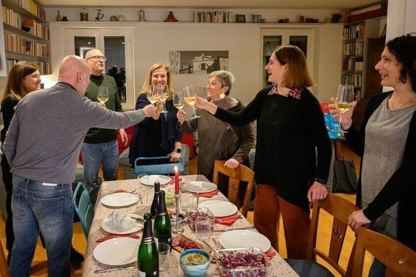 Een groep mensen die met wijn glazen proosten rond een tafel met borden, een fles en een schaal druiven. 2