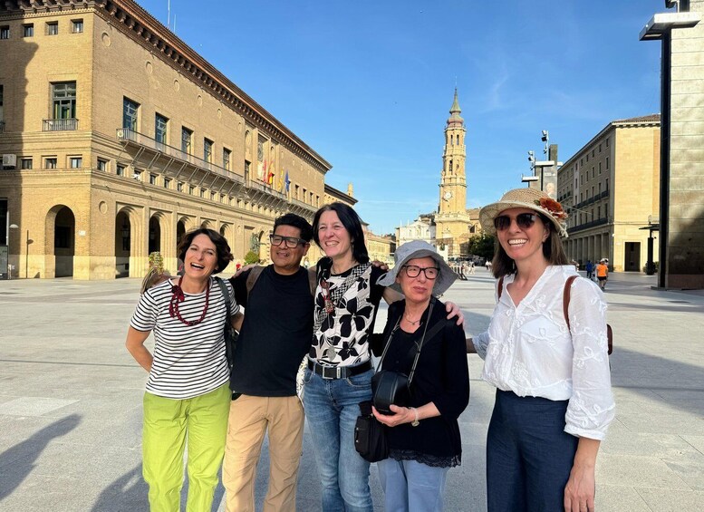 A group of people standing in a plaza with a historic building and a clock tower in the background. 1