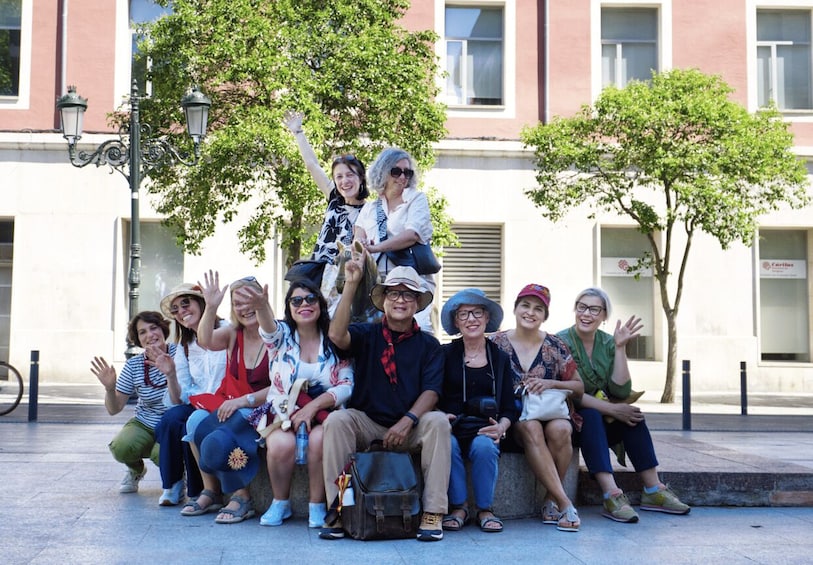 A group of people sitting on a bench in an urban setting with trees and buildings in the background. 1