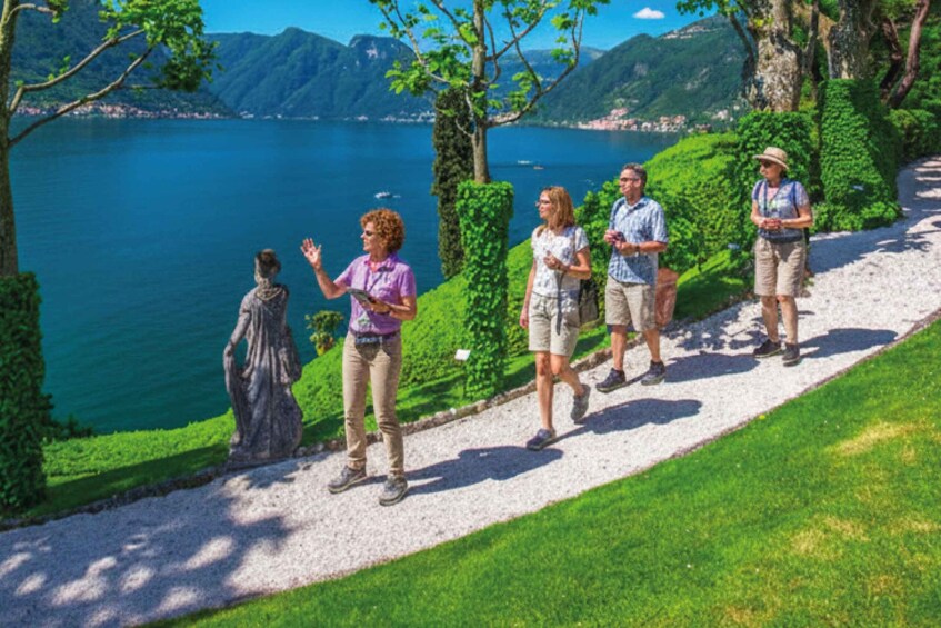 A group of people walking on a gravel path beside a lake with mountains in the background. 3