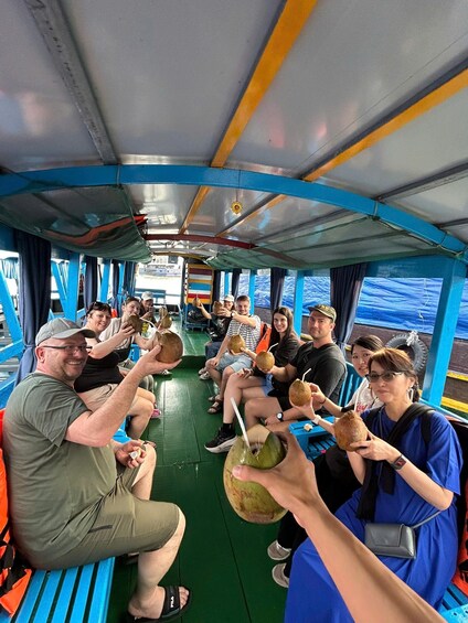 People seated on a boat, holding coconuts. 5