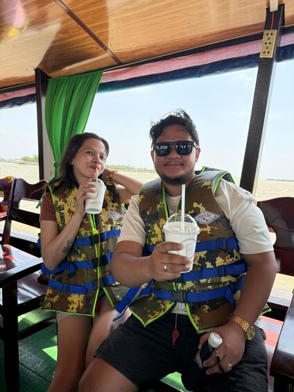 Two people in camouflage life vests sitting at a table on a boat with a green curtain and a view of the water. 3