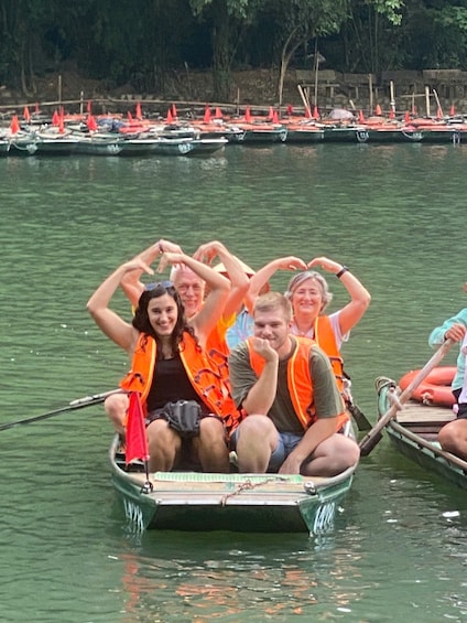 A group of people in a rowboat on a calm body of water, wearing orange life jackets. 2
