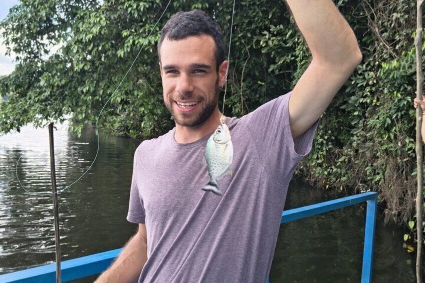 Una persona está de pie junto a un cuerpo de agua con barandilla azul, vestida con una camisa morada y sosteniendo una caña de pescar. 2