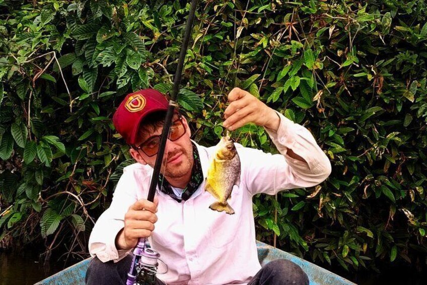 Una persona sosteniendo un pez, con una gorra roja y sentada en un bote. 1