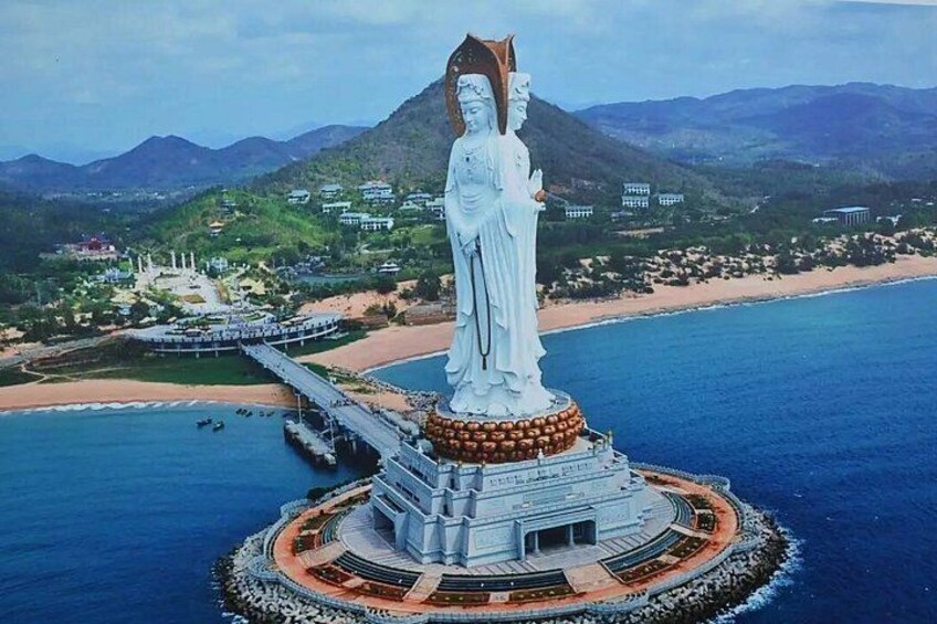 Una estatua blanca grande sobre una plataforma circular rodeada de agua, con un paisaje montañoso al fondo. 1