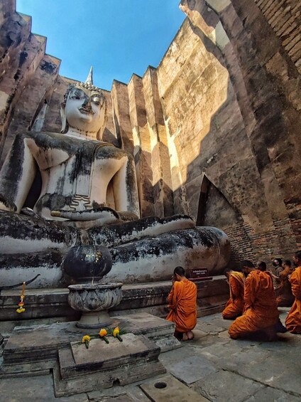 A large reclining Buddha statue in a temple courtyard with monks in orange robes. 4