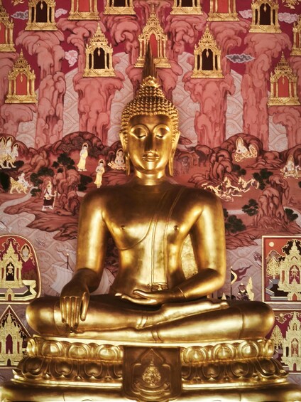 A golden Buddha statue seated in a meditative pose against a backdrop of traditional Thai architecture. 3
