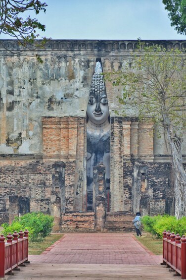 A large Buddha statue carved into a temple wall, with a person walking in the foreground. 1