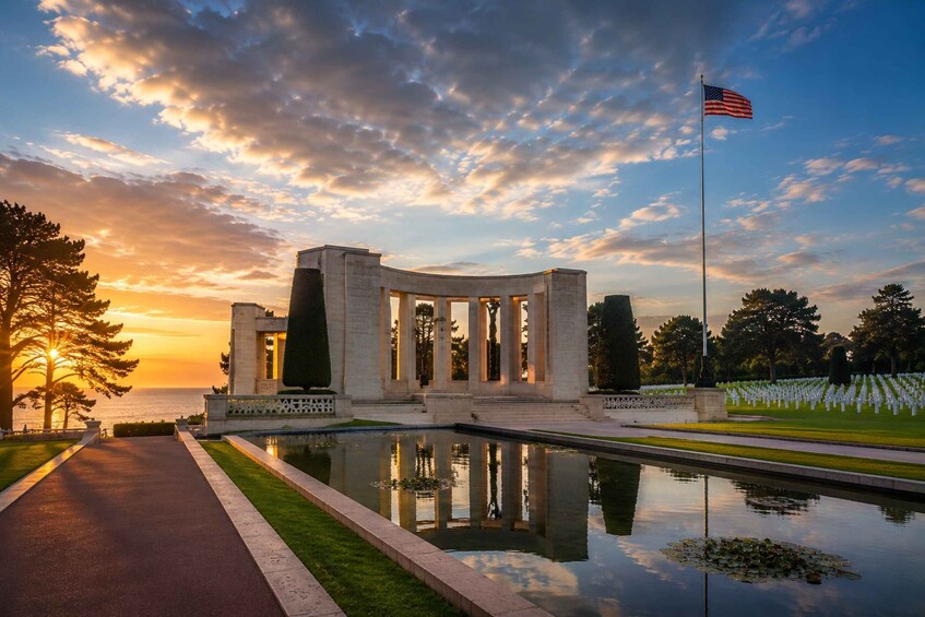 A memorial with columns, a flag, and a reflective pool at sunset. 2