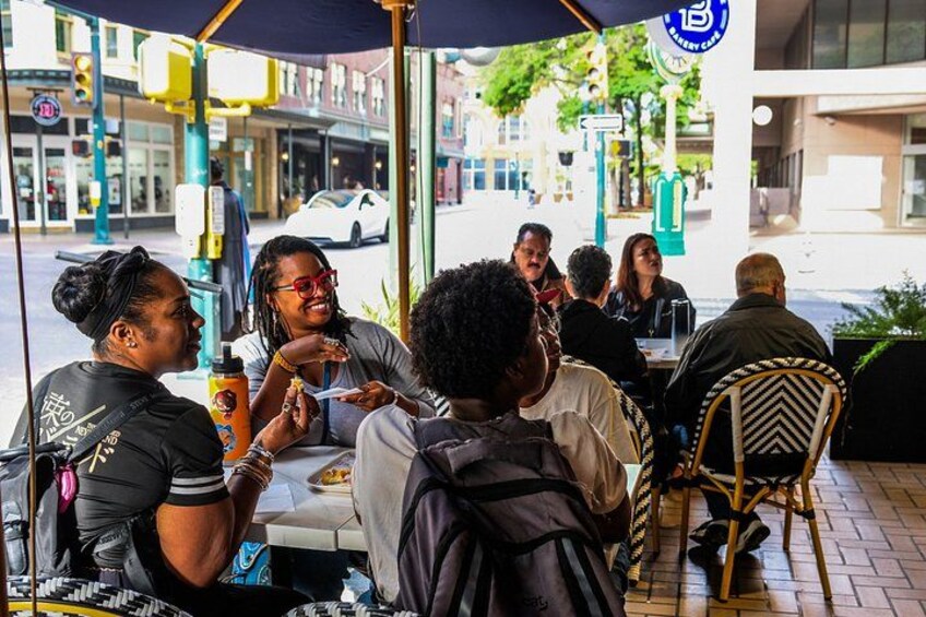 Un grupo de personas sentadas en un café al aire libre con una sombrilla azul. 4