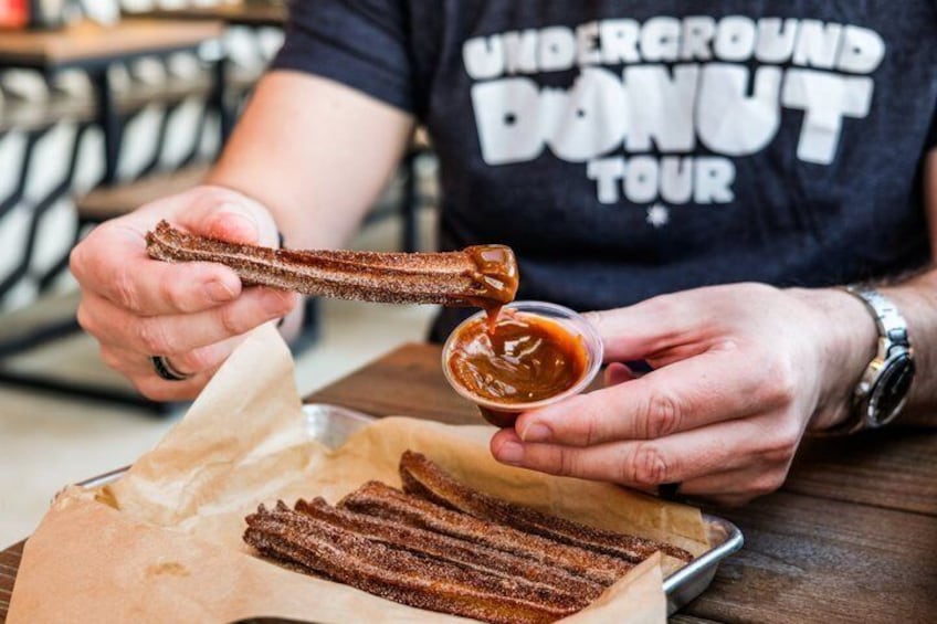 A person holding a churro and dipping it into a sauce. 4