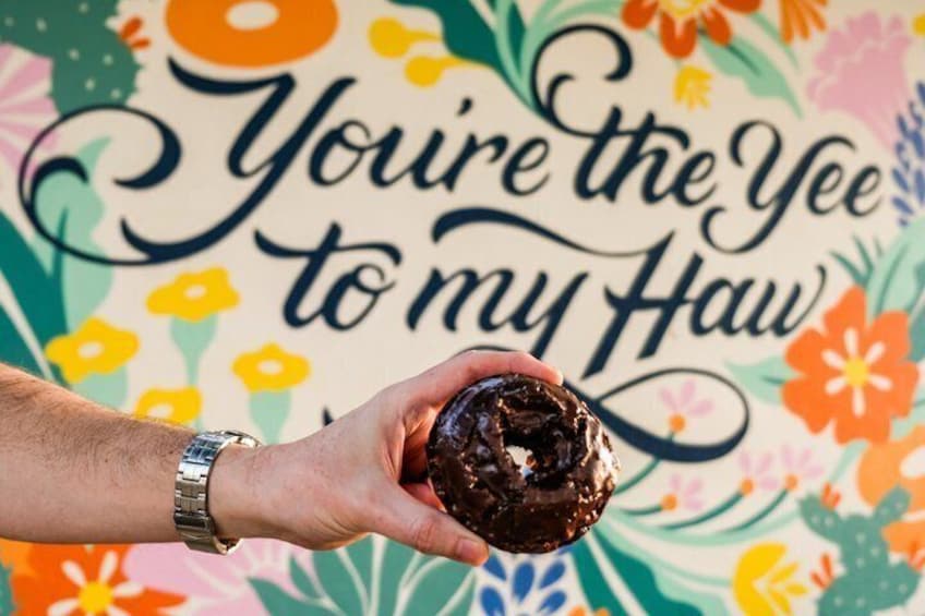 A hand holding a chocolate-covered donut with a colorful floral background and the text 'You're the Yee to my Haw'. 5