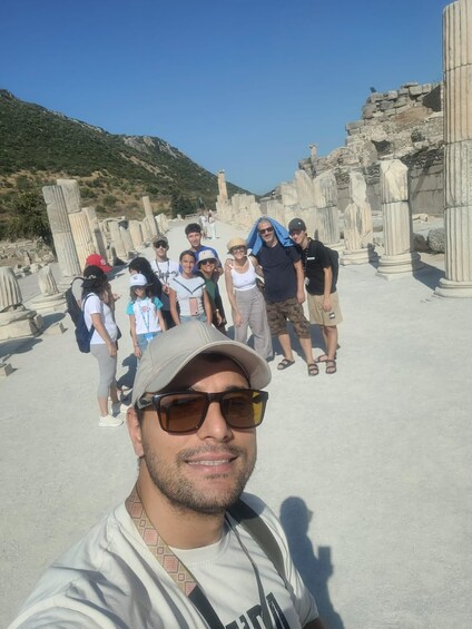A group of people at an ancient ruin site with columns and a mountainous backdrop. 2