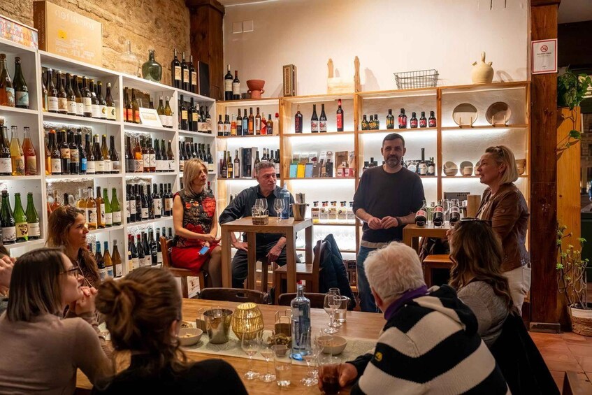 A group of people seated at a table in a wine shop with shelves of wine bottles in the background. 3