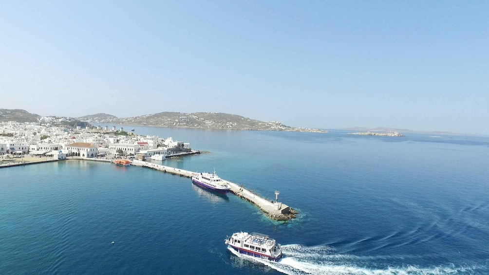 A coastal town with white buildings, a pier, and two boats on the water. 1
