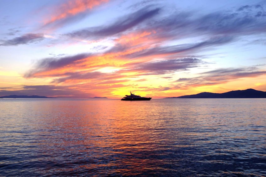 A sunset over calm waters with a ship in the distance and mountains on the horizon. 3