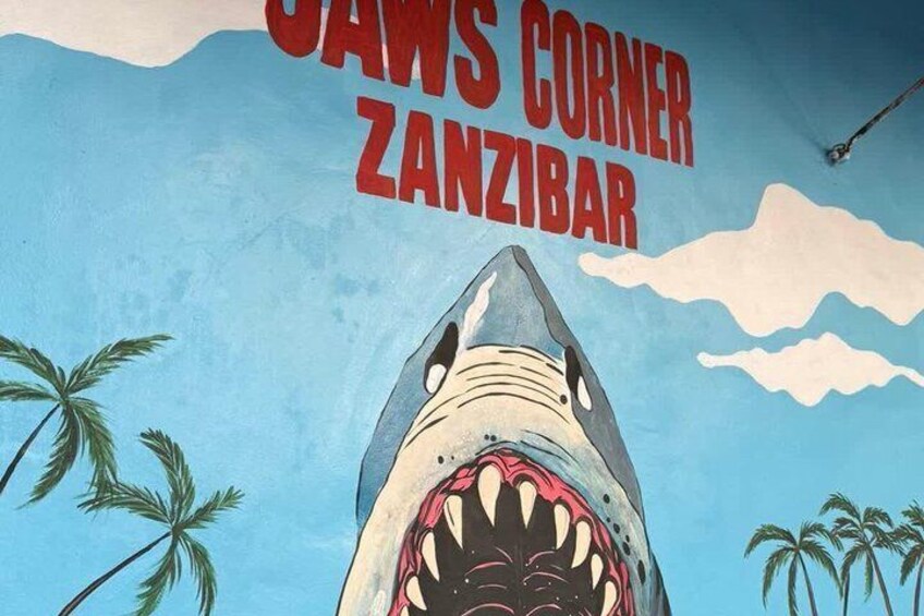Un murale a forma di squalo con il testo 'Jaws Corner Zanzibar' e palme. 5