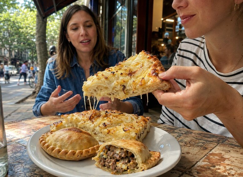 A person holding a slice of a cheesy, baked dish, with a plate of similar food and a partially eaten meat-filled pastry on the table. 4