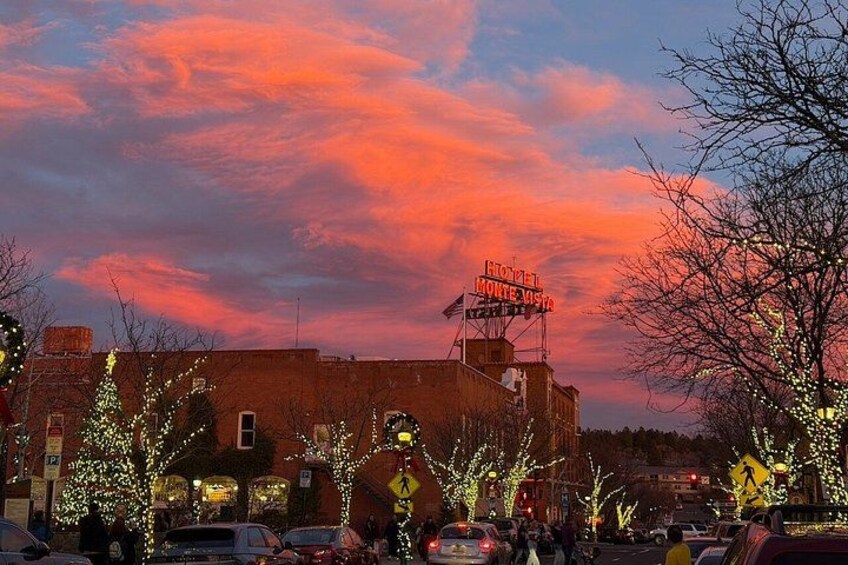 Un atardecer con un cielo en tonos rosados y morados, un edificio con un letrero de neón y árboles decorados con luces. 3