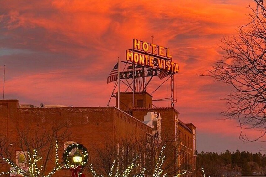 Un hotel llamado 'Monte Vista' con un letrero de neón, rodeado de árboles desnudos y un cielo al atardecer. 2