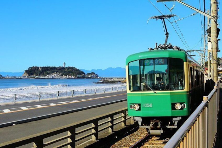A green tram with the number 1052 on a track near a beach with a distant island. 1