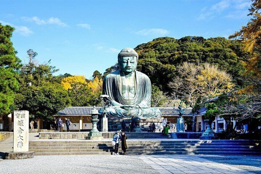 A large Buddha statue in a temple setting with steps leading up to it, surrounded by trees and traditional architecture. 1