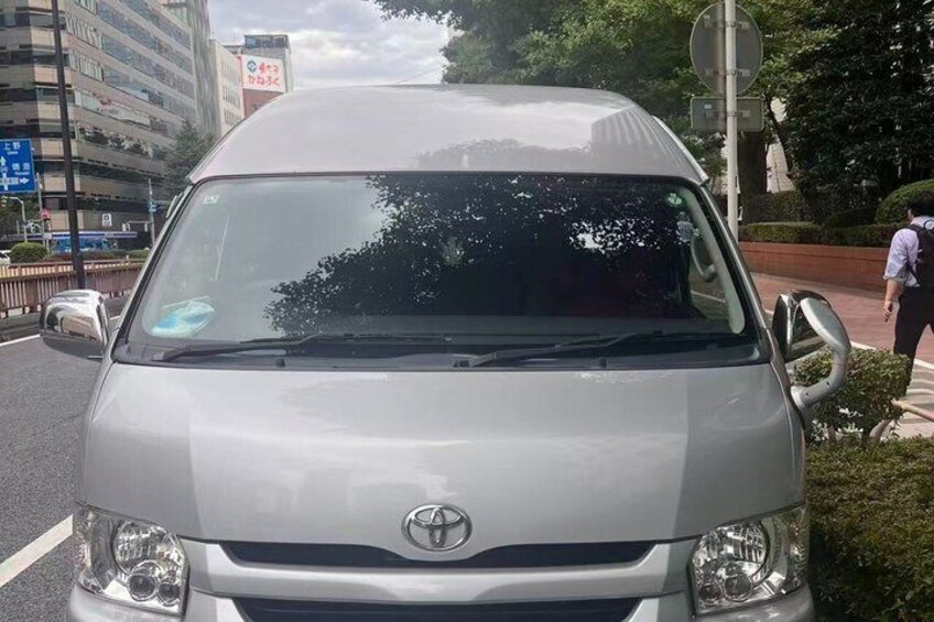 Ein silberner Toyota-Van steht auf einer Stadtstraße, im Hintergrund sind Gebäude und Grünflächen zu sehen. 3