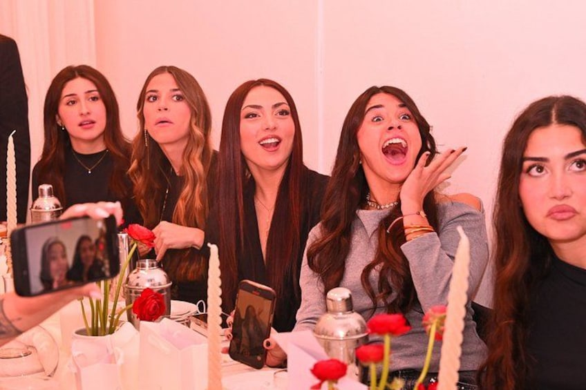 Un gruppo di persone sedute a tavola, con candele, fiori e una cornice per foto. 2