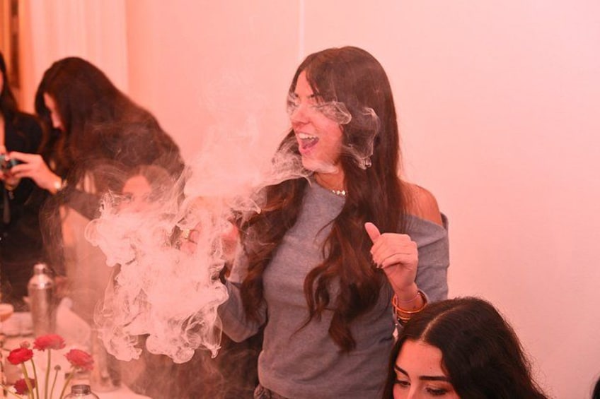 Una persona che espira fumo, con sullo sfondo sfocate altre persone. 3