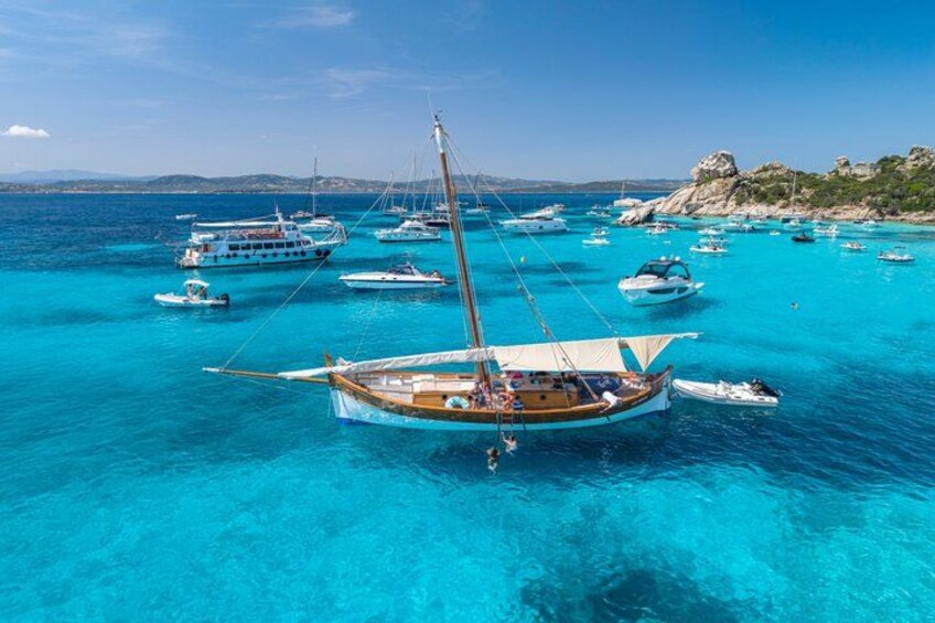Une mer d’un bleu profond où sont amarrés plusieurs bateaux, une côte rocheuse et des montagnes lointaines. 5