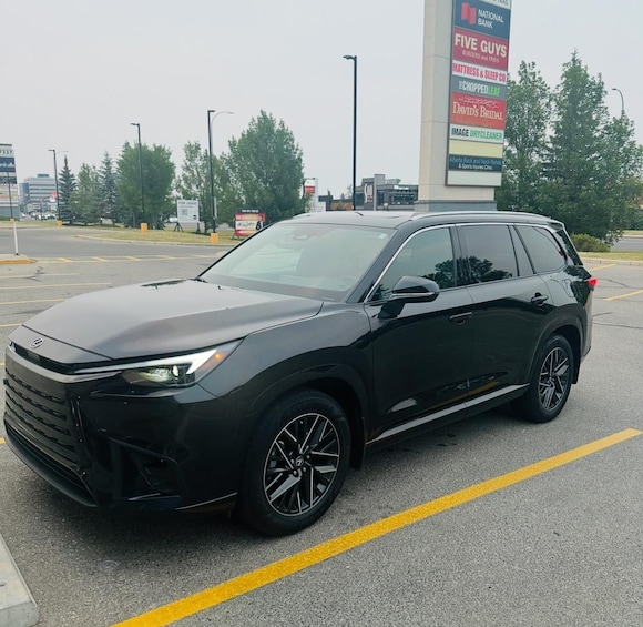 A black SUV parked in a lot with a large sign advertising various businesses in the background. 2