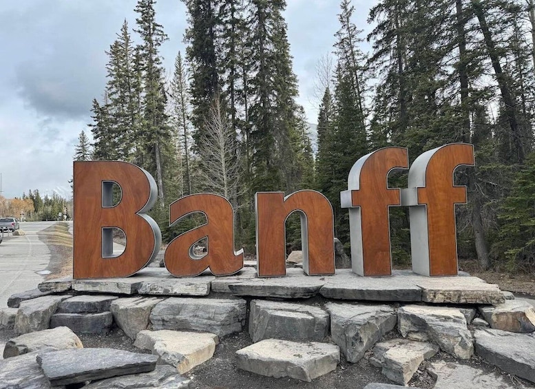 Large wooden letters spelling 'Banff' on a stone base, surrounded by trees. 1