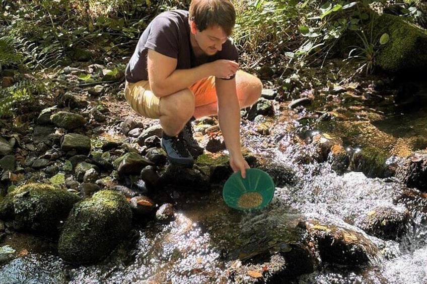A person crouching by a stream with a green bowl. 1