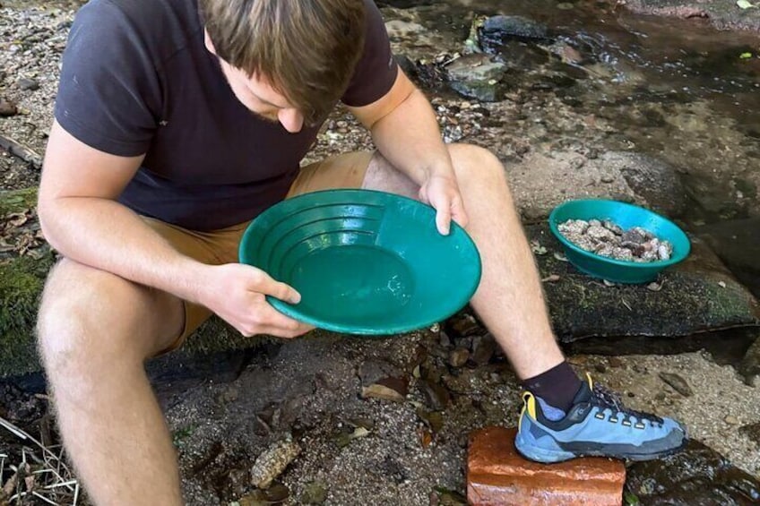 A person sitting on a rock by a stream, holding a green bowl. 5