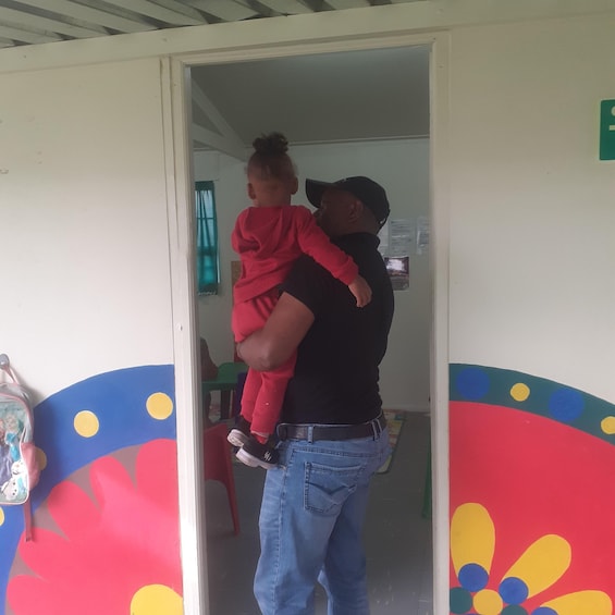 A man carrying a child in a doorway with colorful wall art. 5
