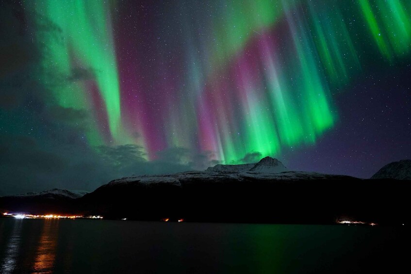 The Northern Lights over a snowy landscape with a lake and distant lights. 1